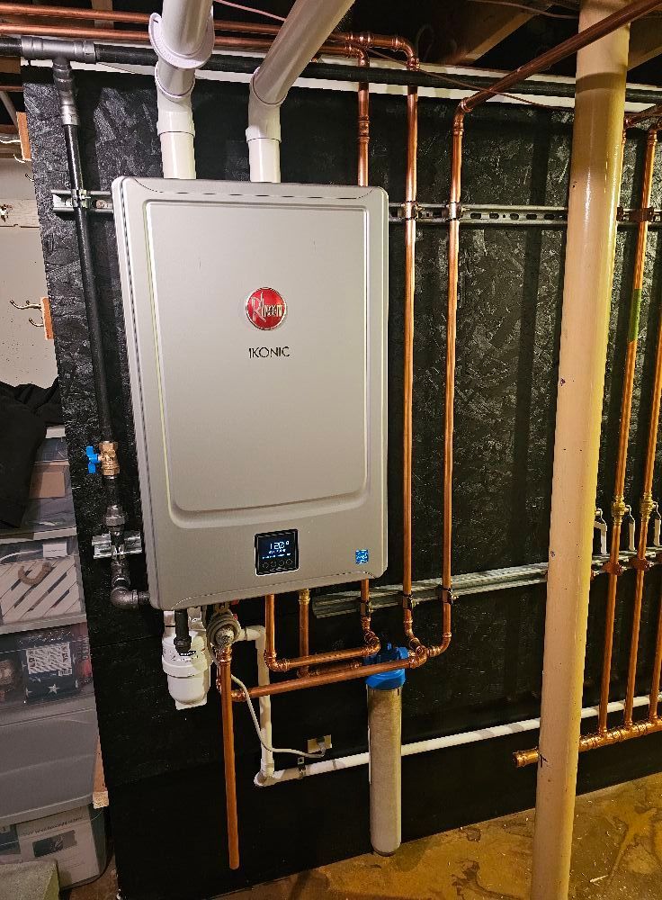 Rheem tankless water heater with copper pipes and a water filter installed in a basement.