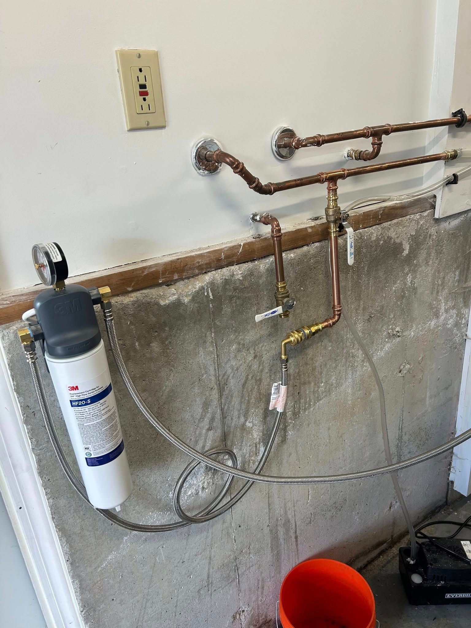 Plumbing with water filter and copper pipes against a concrete wall.