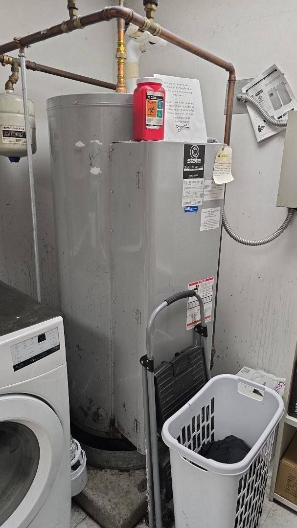 Water heater in a laundry room with a washing machine and laundry basket.