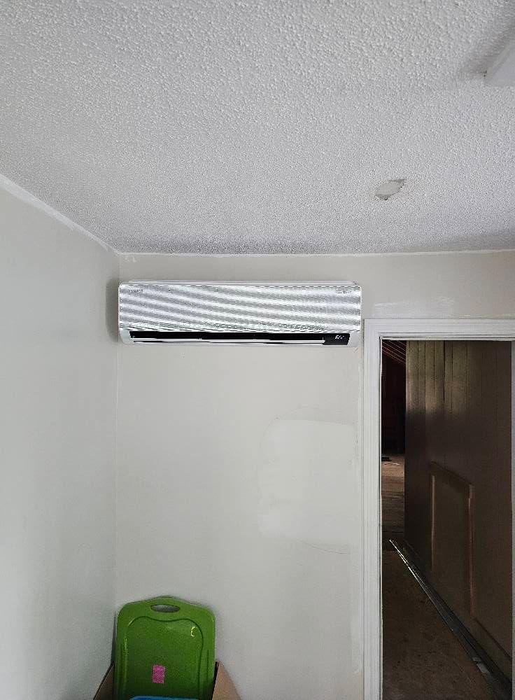 Air conditioning unit mounted on a white wall above a green storage container; doorway to the right.