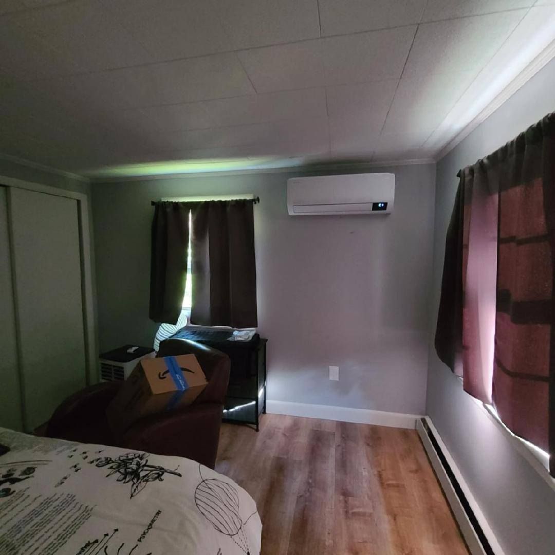 Bedroom with AC unit, closet, bed, brown curtains, and wood-look flooring.