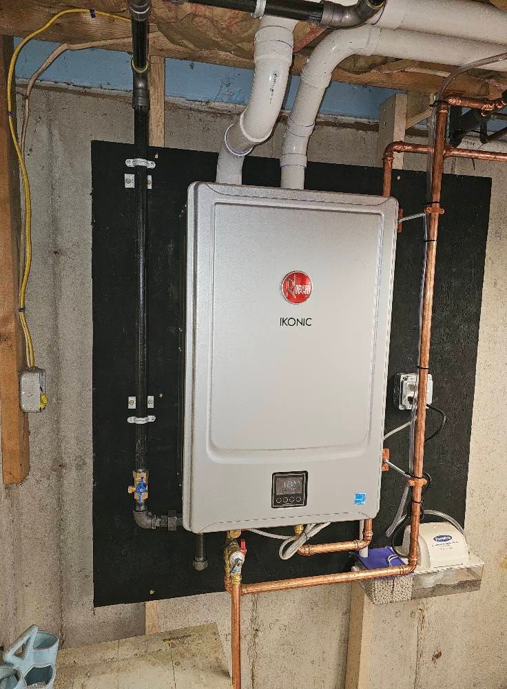 Rheem tankless water heater installed in a basement, with copper pipes and a black backing.