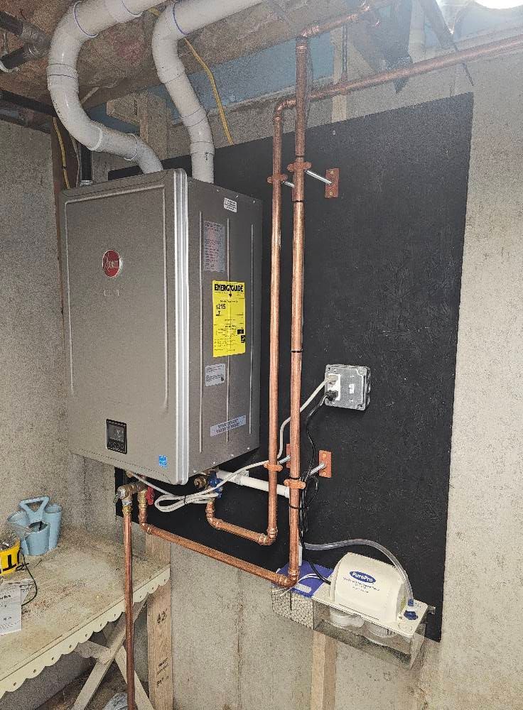 Wall-mounted water heater with copper pipes and electrical components installed in a basement setting.