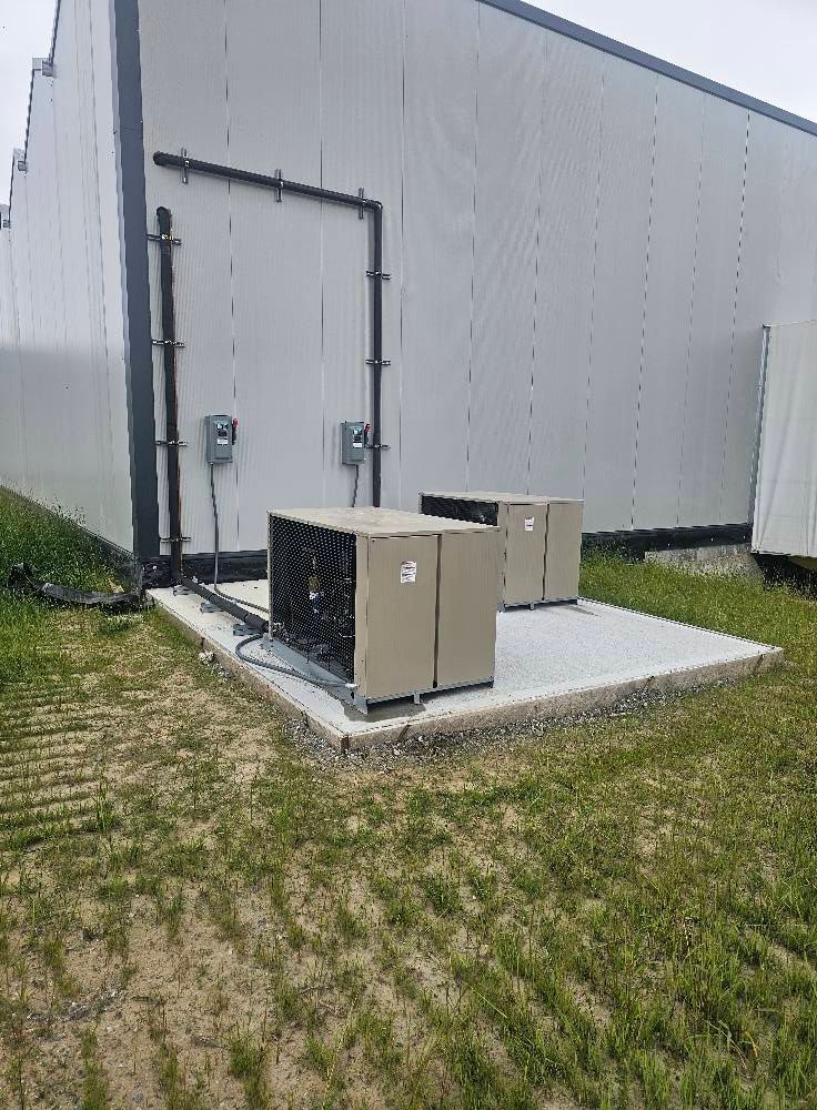 Two beige HVAC units on concrete pad outside a white industrial building.