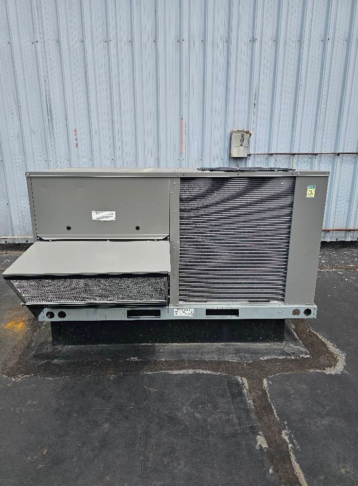 A gray rooftop HVAC unit on a concrete surface, with a corrugated metal wall in the background.