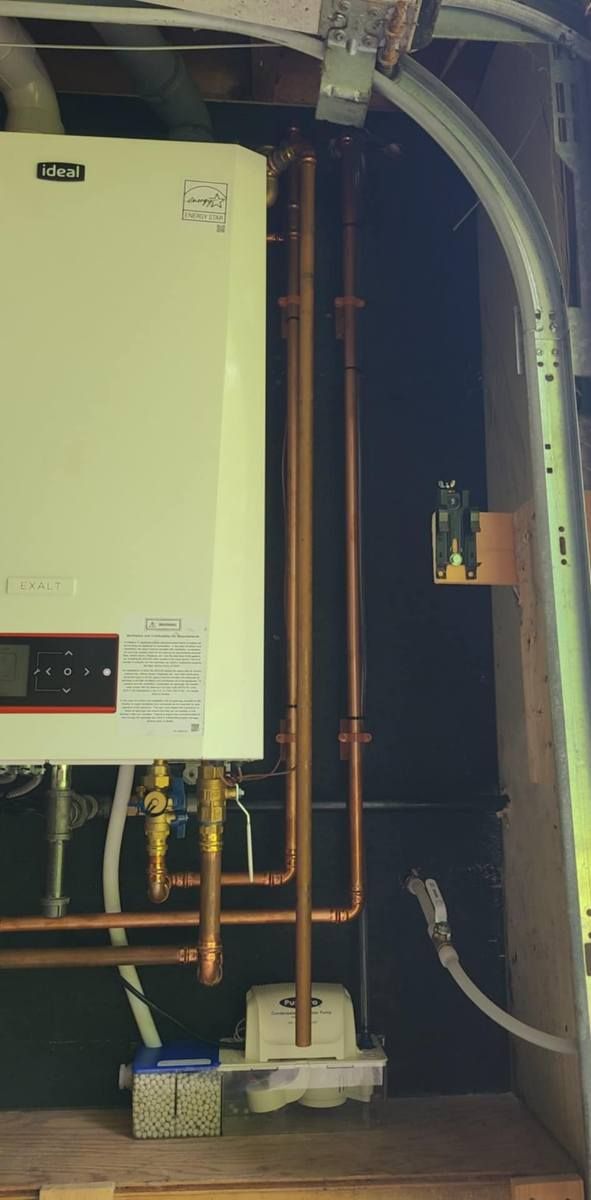 A wall-mounted, white boiler with copper pipes and fittings. Located inside a wooden structure.