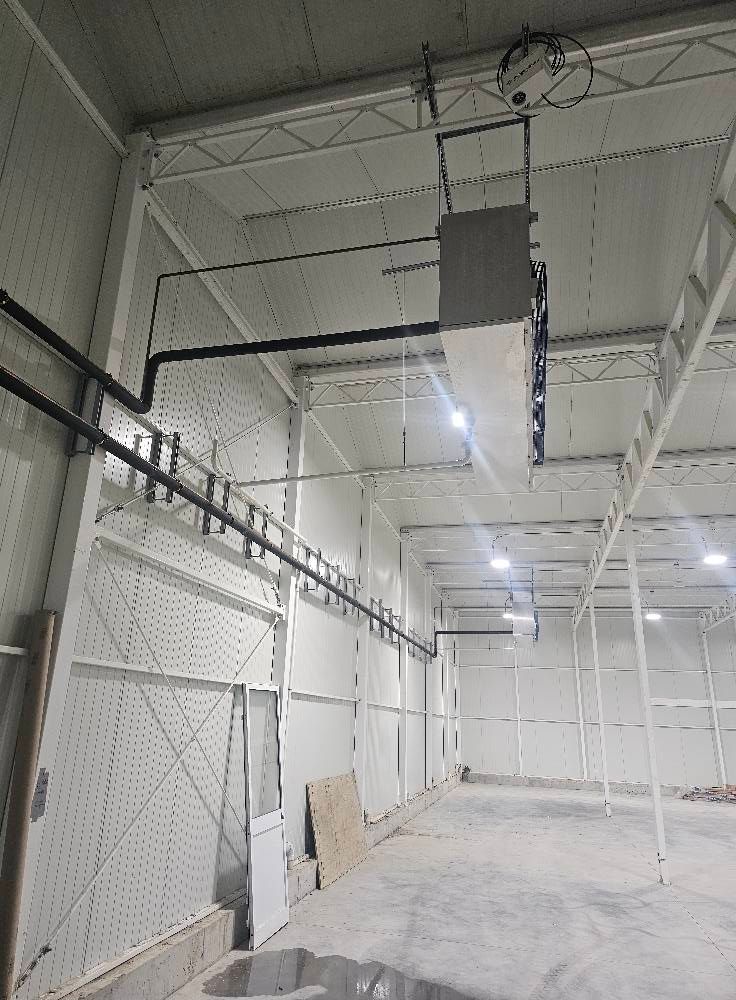 Interior view of an industrial building with overhead HVAC and lighting fixtures, concrete floor, and white walls.