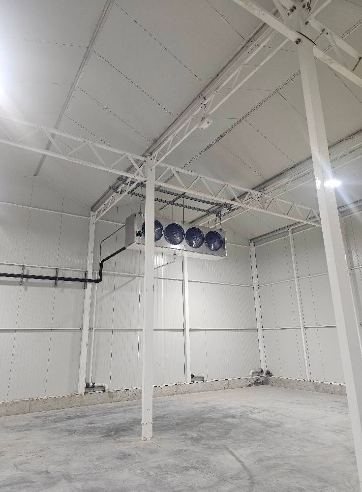 Interior of a large, white warehouse with ceiling fans and metal support beams.