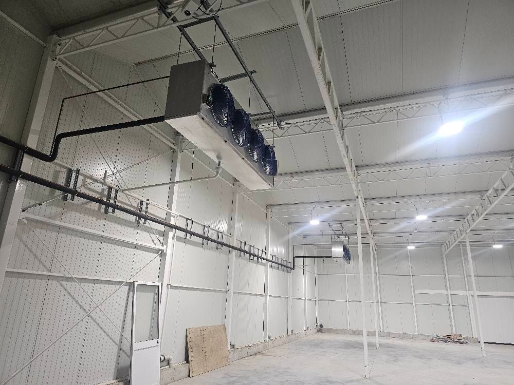 Industrial interior with cooling units suspended from the ceiling and pipes along the walls.