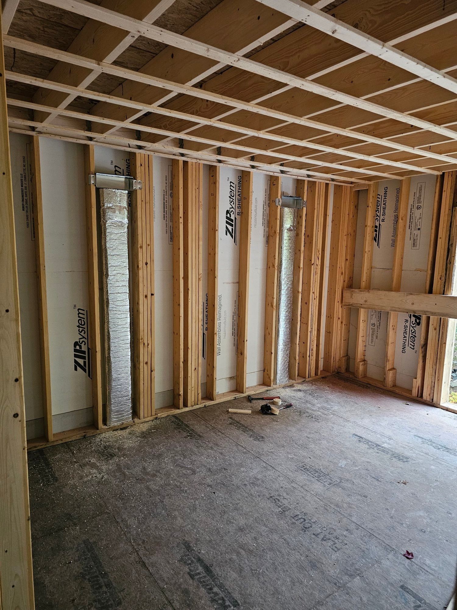 Interior of a room under construction, with wooden studs, insulation, and unfinished ceiling.