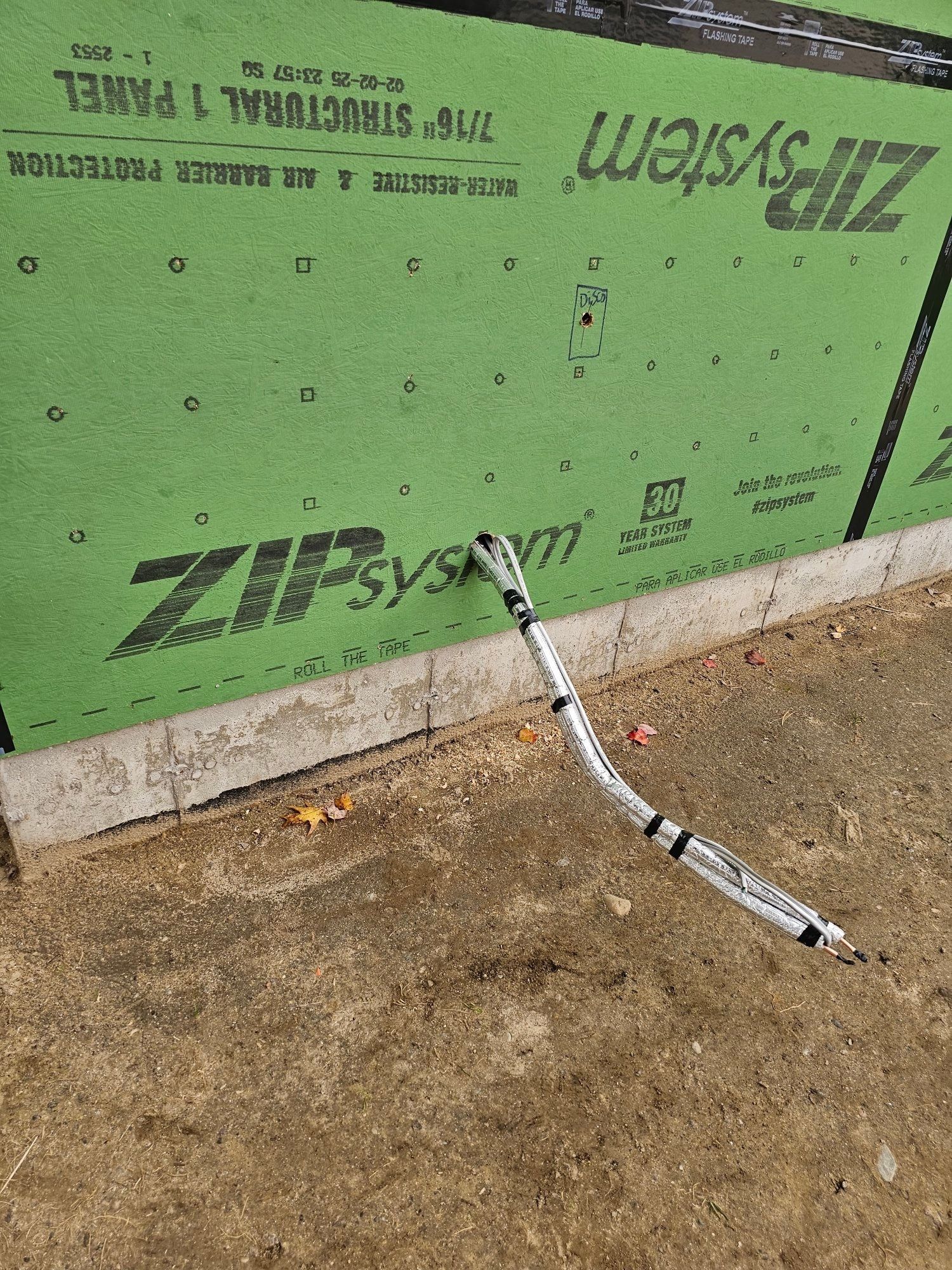 A gray electrical cable lying on a dirt ground, against a green wall labeled 