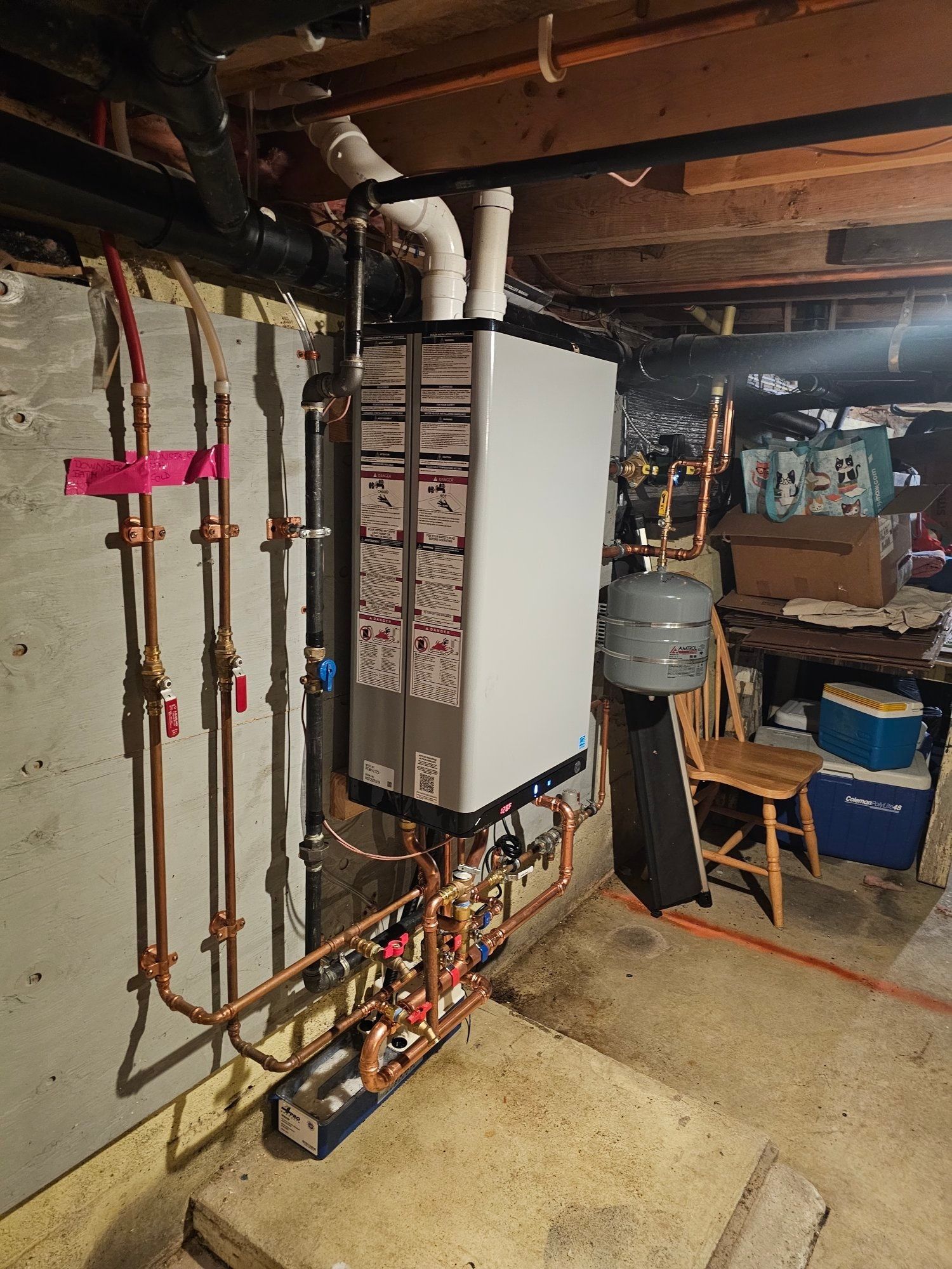 A white water heater with copper pipes in a basement.