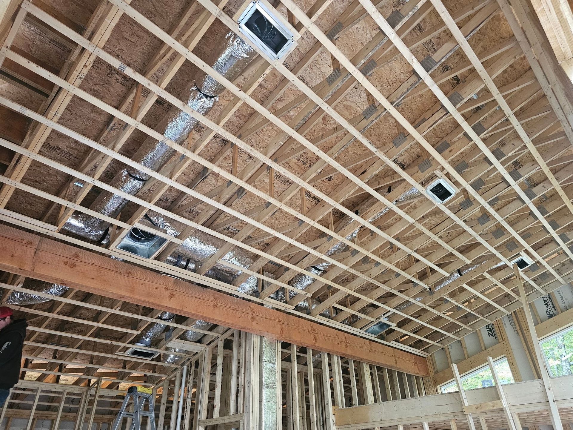 Interior view of a building under construction, showing wooden framing, ductwork, and ceiling vents.
