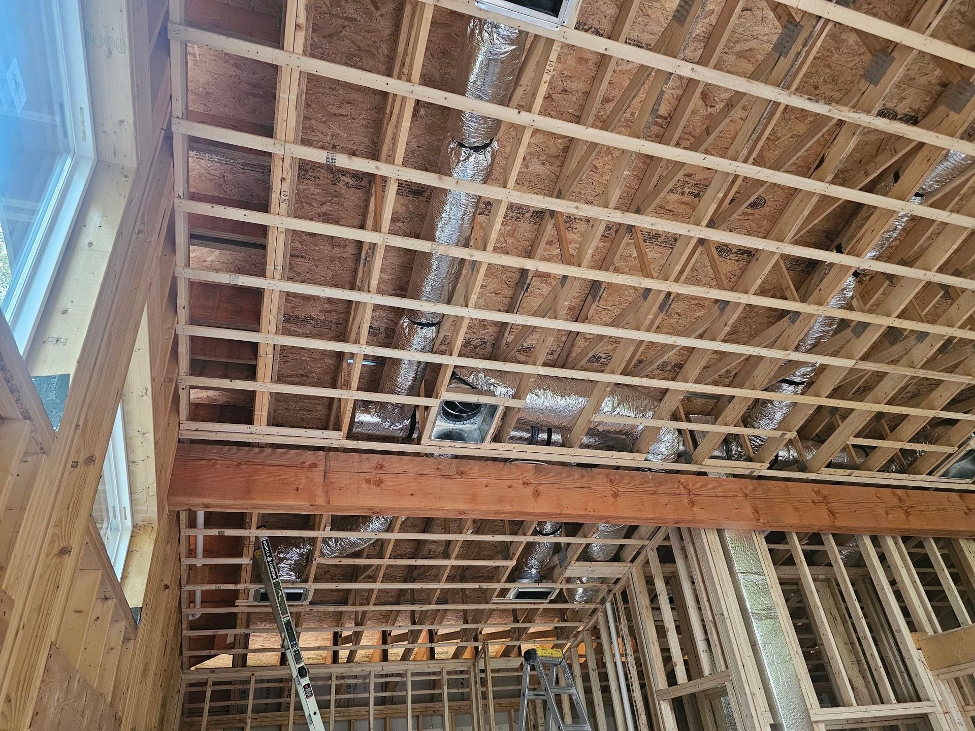 Interior of a building under construction, showing exposed wooden beams, ductwork, and window frames.