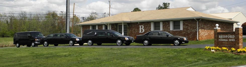 A line of black funeral vehicles parked in front of a brick building with a 