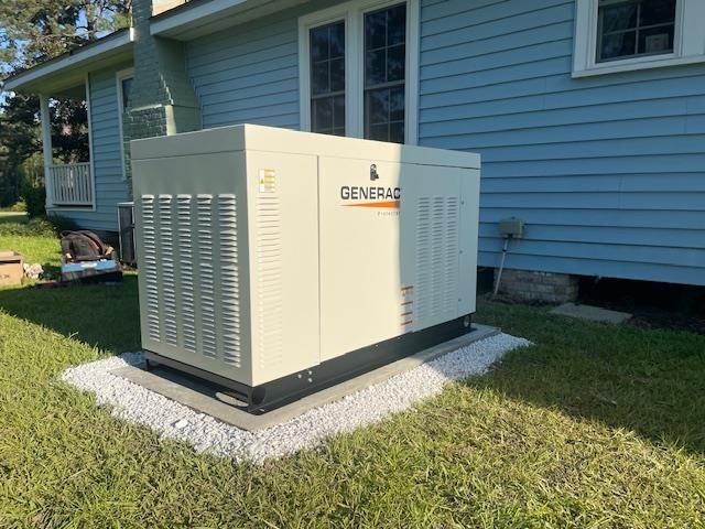 Large Generac generator in beige casing on a gravel base next to a blue house.
