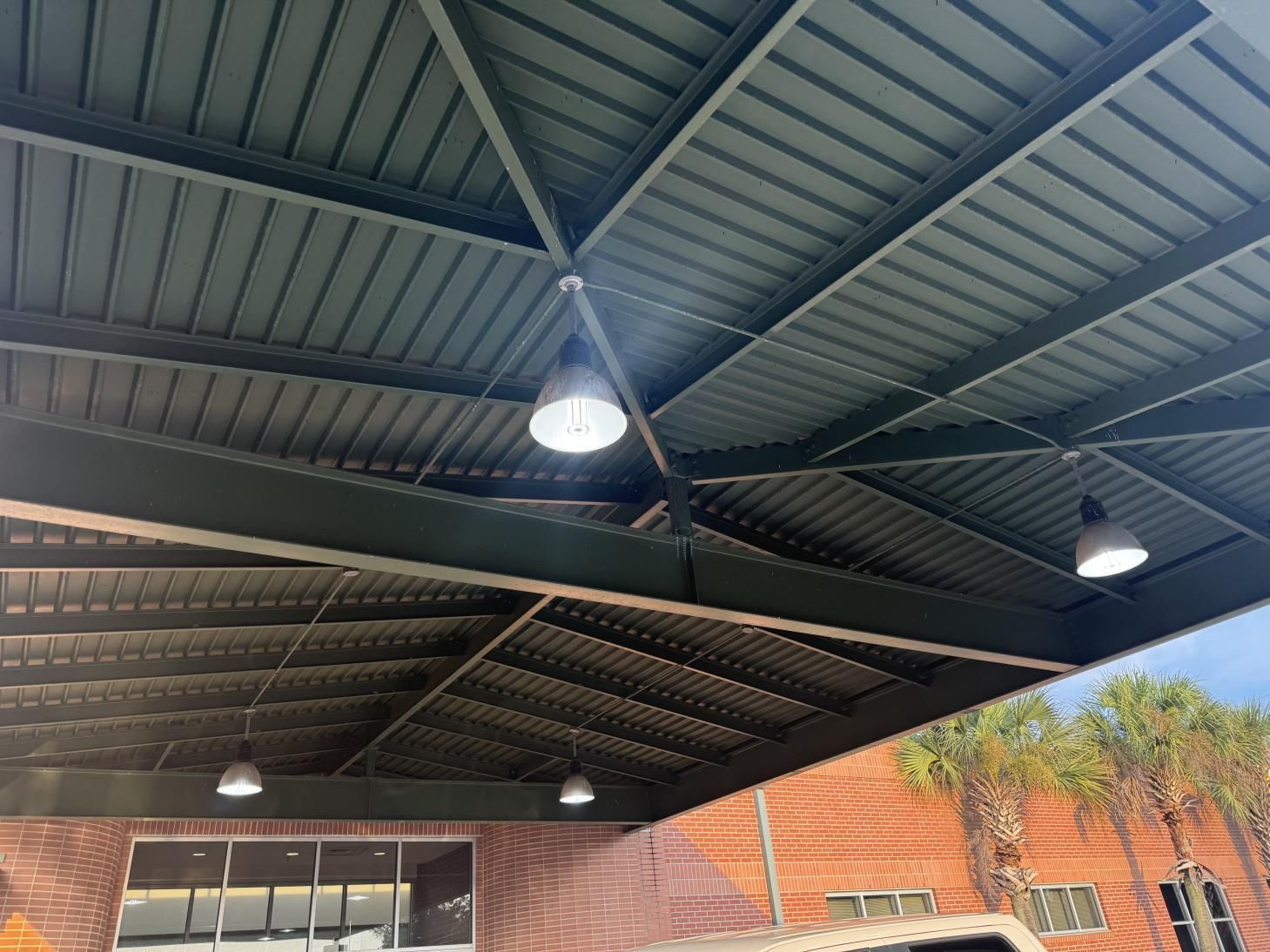 Metal roof with hanging lights; brick building exterior with trees.