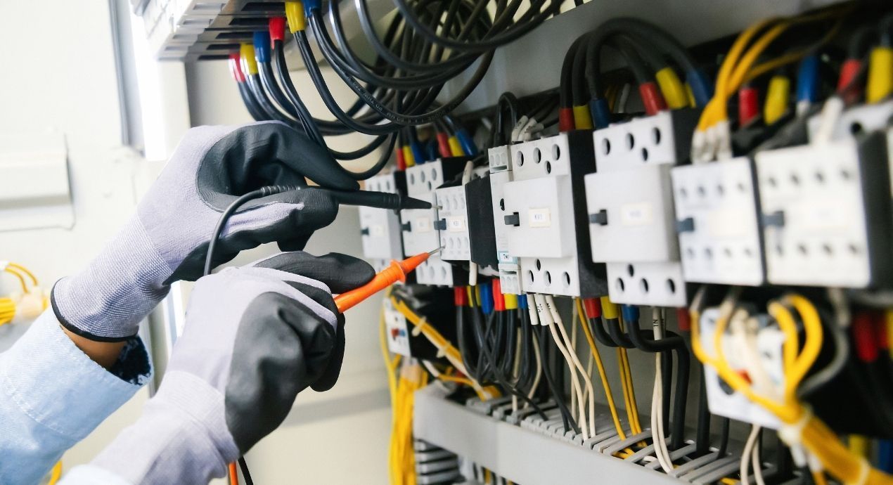 Electrician testing electrical panel with a multimeter; wires, black gloves, close-up.