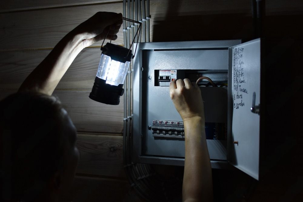 Person using a lantern to illuminate an open electrical panel in a dark setting, flipping a switch.