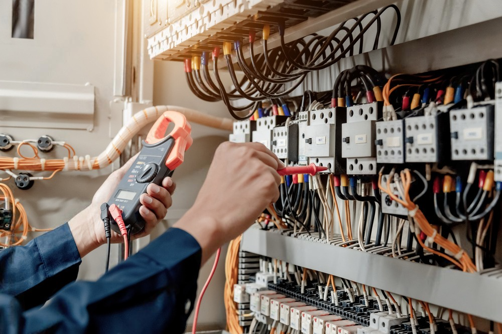 An electrician uses a multimeter to inspect electrical wiring in a control panel.