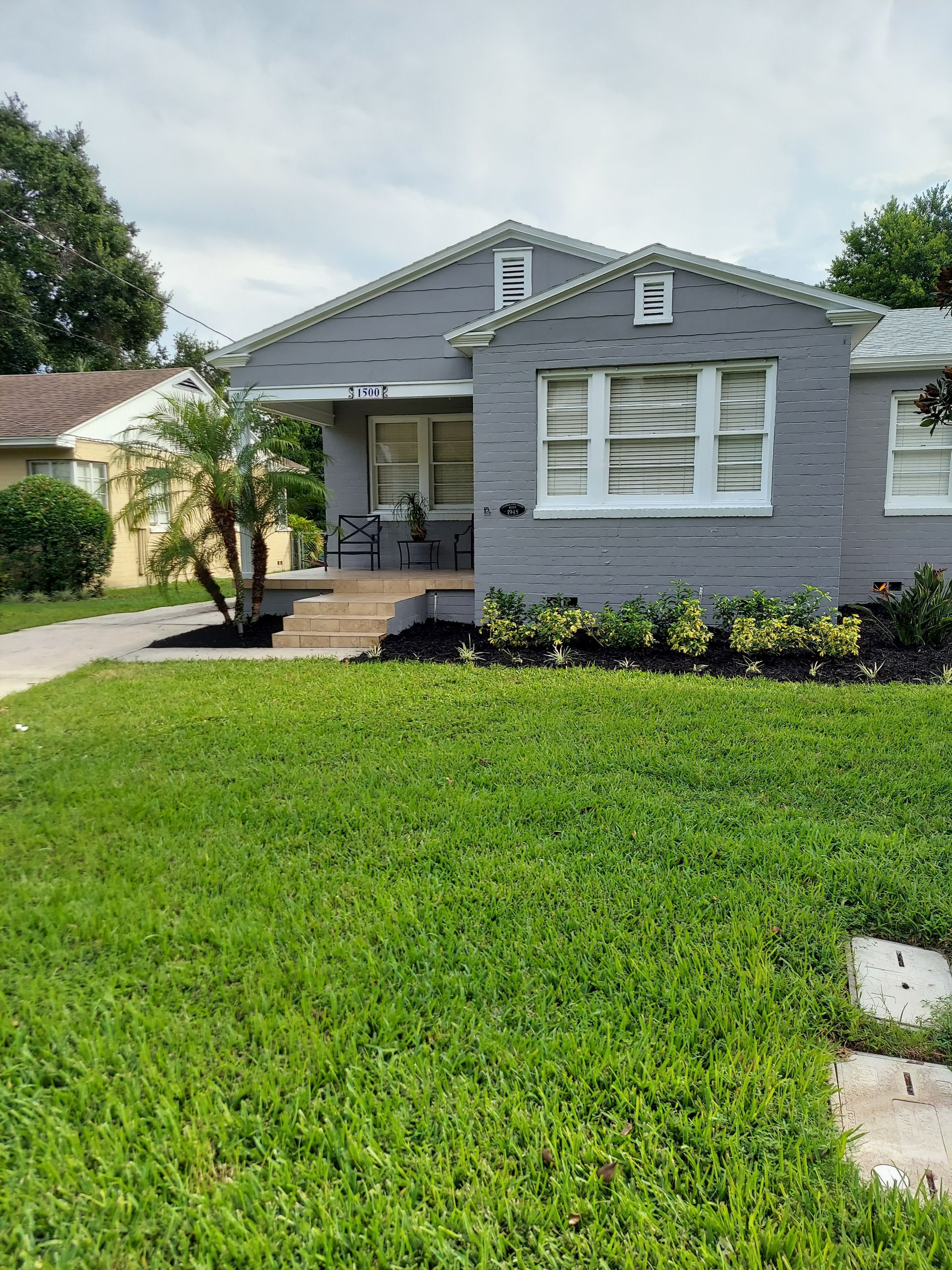A gray house with a lush green lawn in front of it.