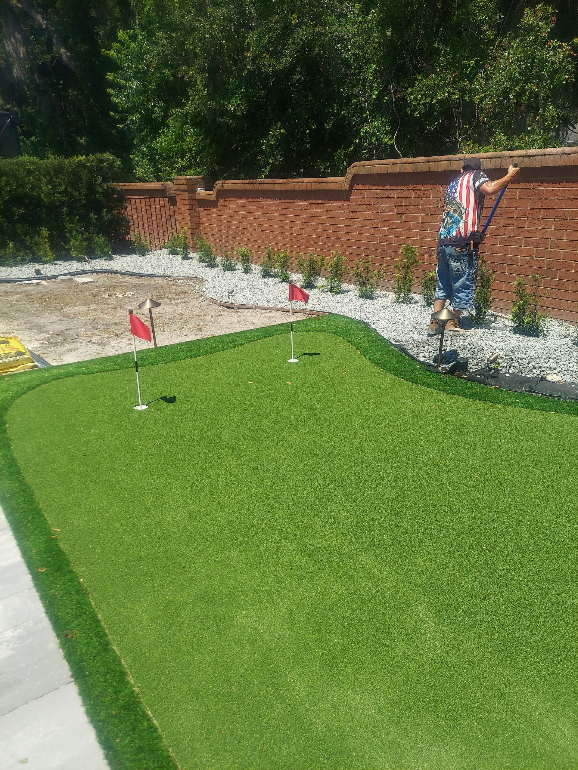 A man is standing on top of a lush green lawn next to a brick wall.