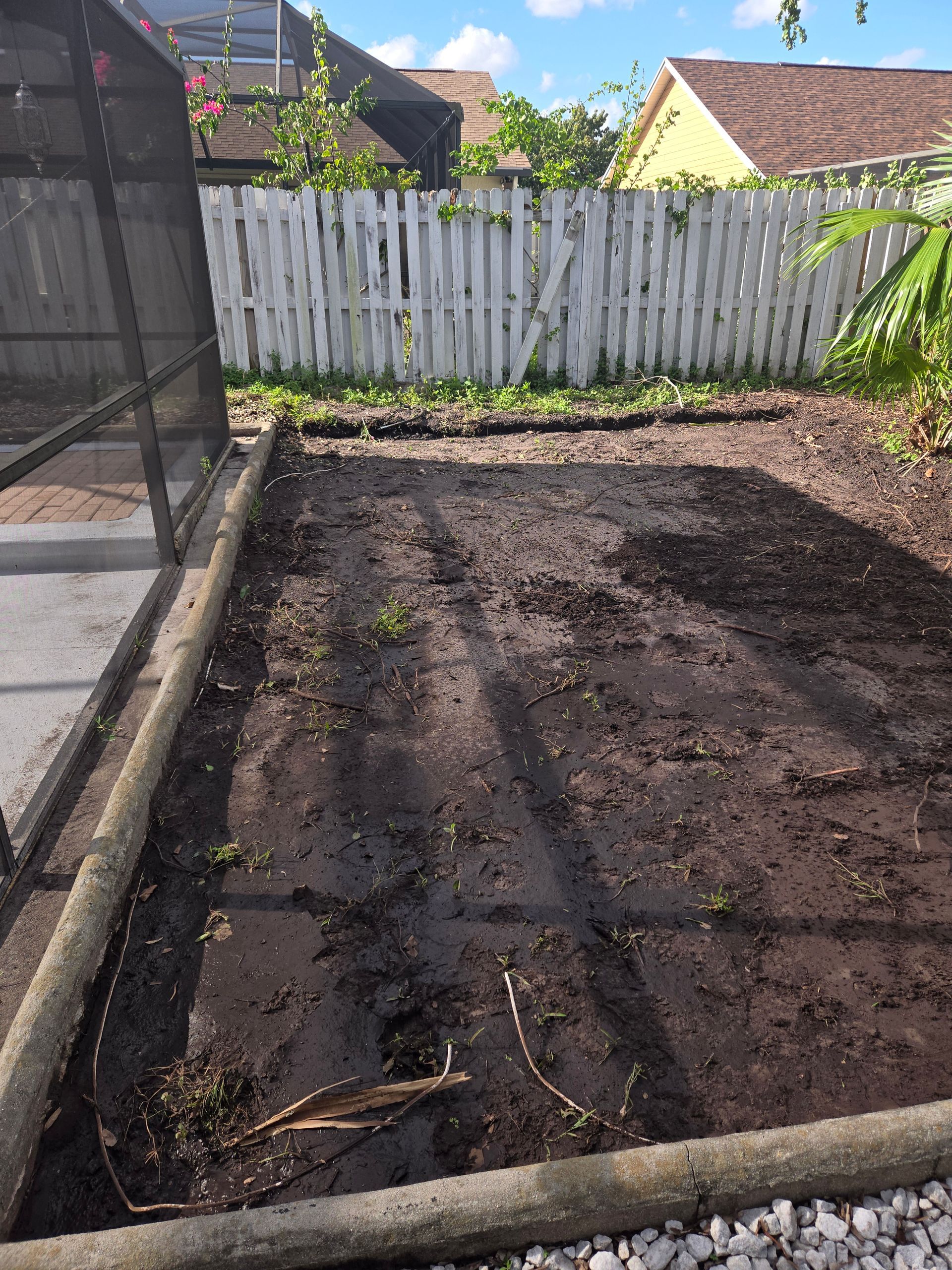 A muddy yard with a white fence in the background