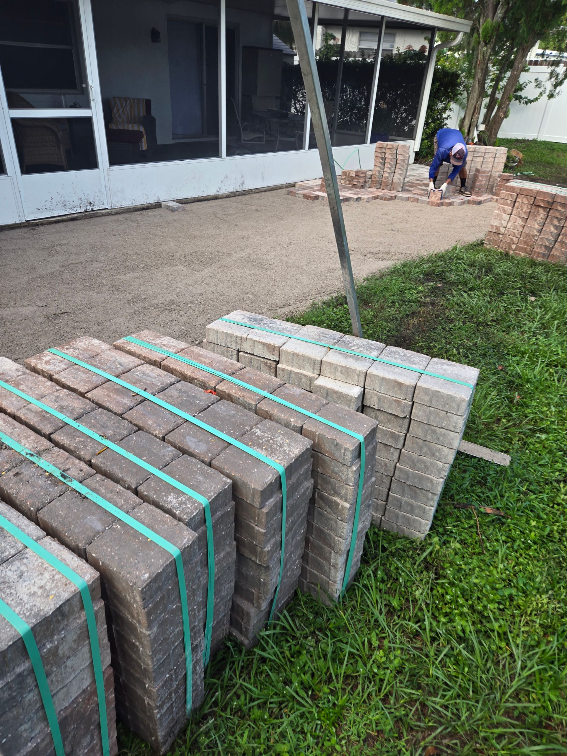 A bunch of bricks are sitting on the grass in front of a house.