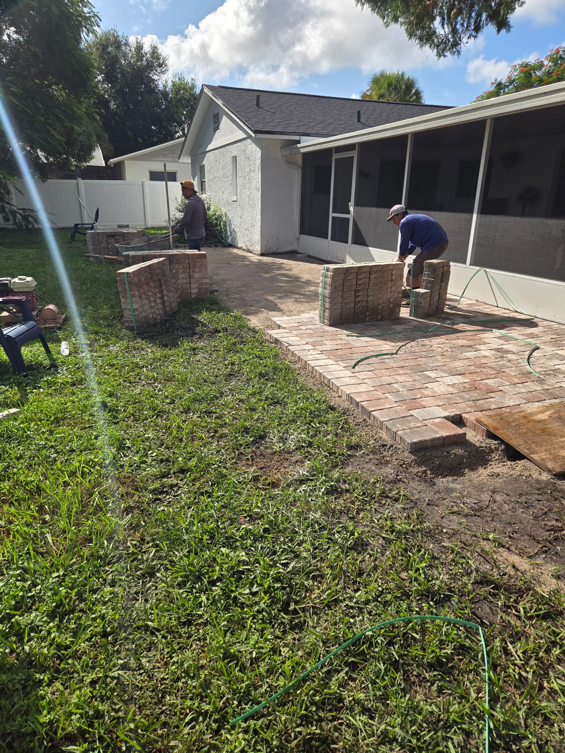 A man is working on a brick patio in front of a house.