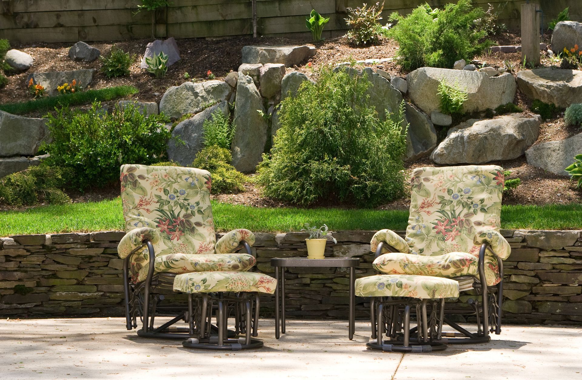 Two chairs and a table on a patio in front of a rock wall
