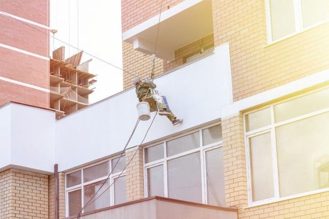 Worker suspended on ropes cleaning a building exterior near sunlit windows