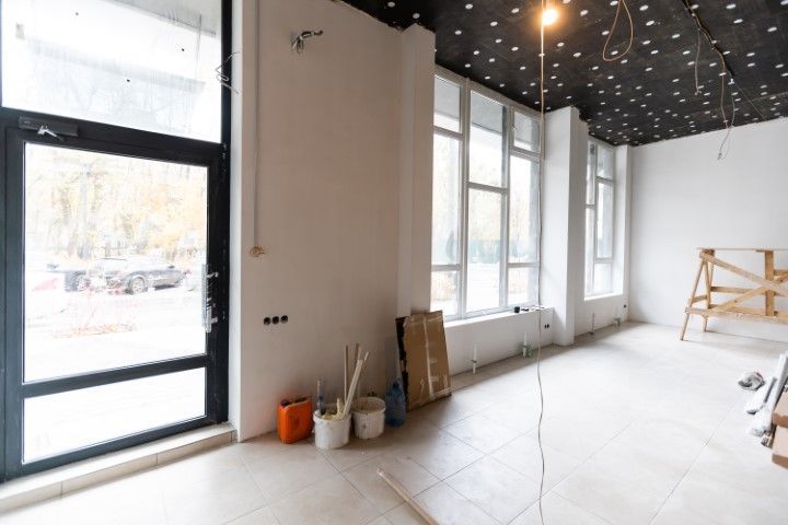Empty, unfinished room with large windows, white walls, and cleaning supplies near the entrance