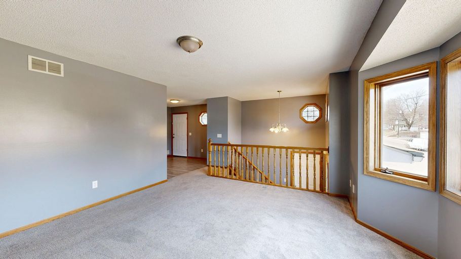 Empty beige living room with carpet, railing, and large window overlooking snowy trees