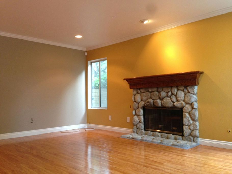 Empty living room with hardwood floors, beige walls, a small window, and a stone fireplace.