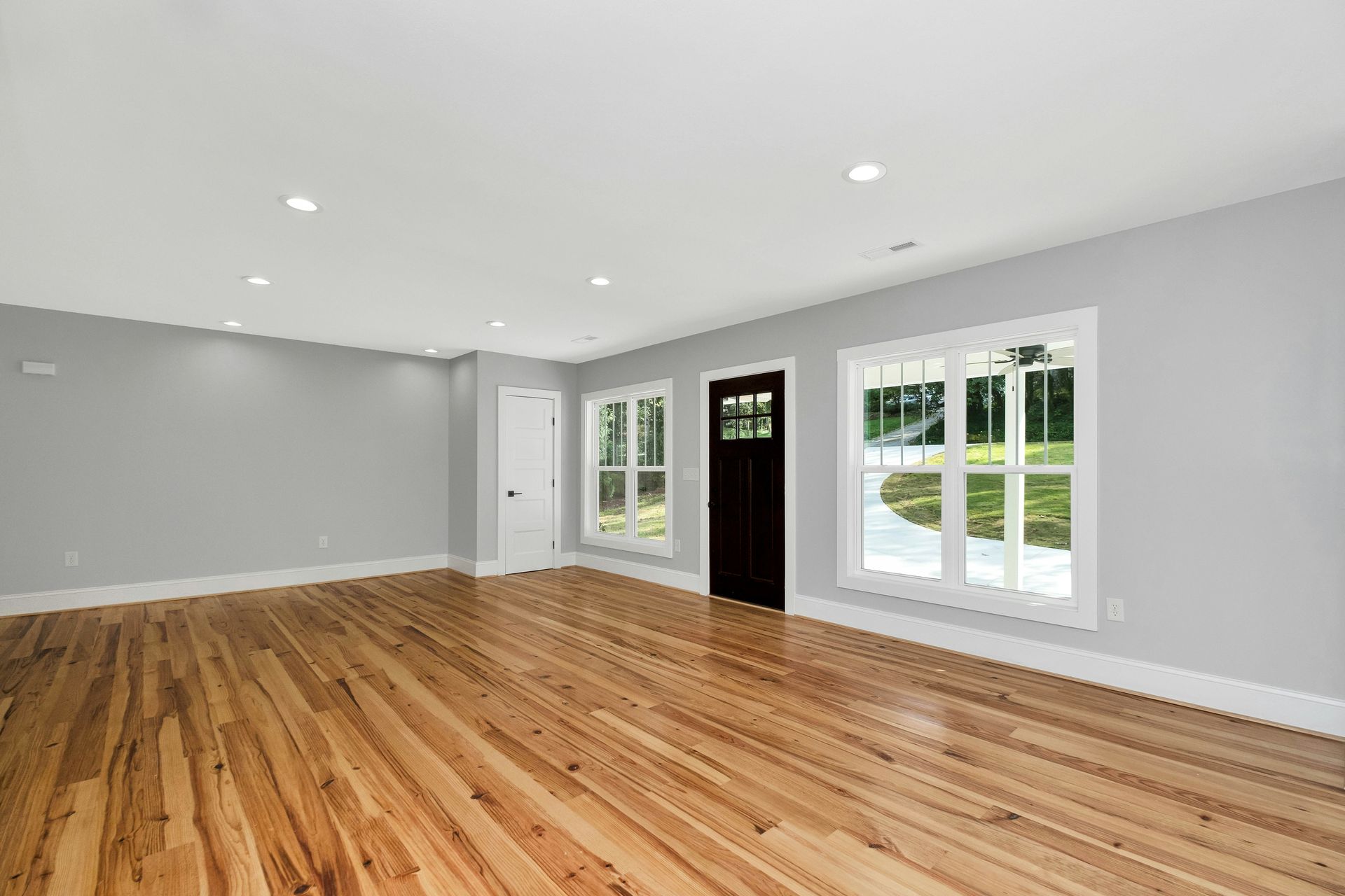 Bright empty room with hardwood floors, gray walls, recessed lights, and large windows and glass doors.