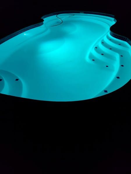 A large swimming pool is lit up at night with blue lights.