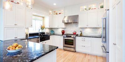 A kitchen with white cabinets , black counter tops , stainless steel appliances and a bowl of fruit on the counter.