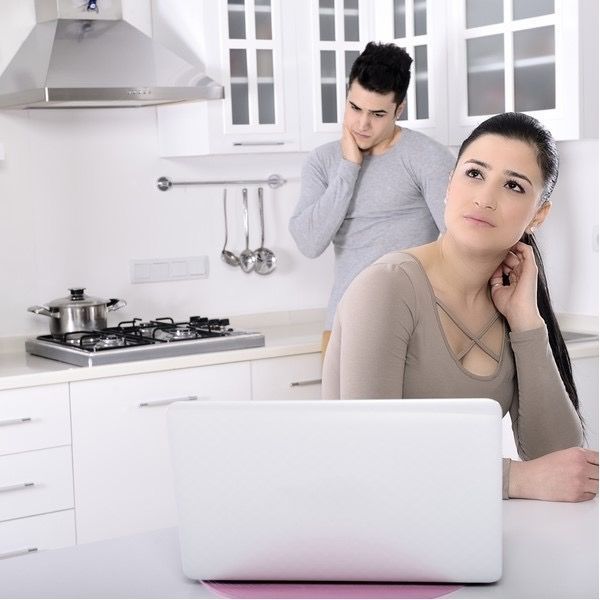 A woman sits in front of a laptop in a kitchen
