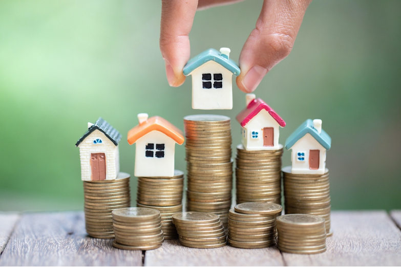 A person is putting houses on top of stacks of coins.