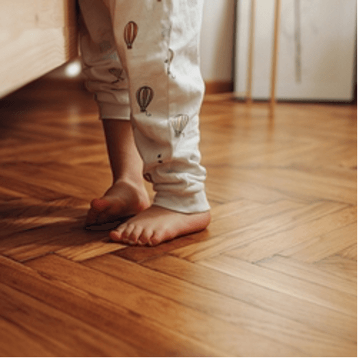 A child 's bare feet are standing on a wooden floor.