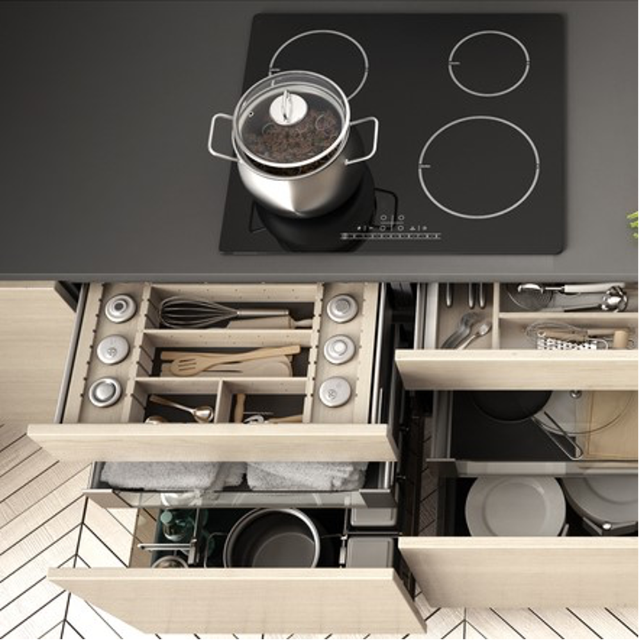 A pot sits on top of a stove next to a drawer full of pots and pans