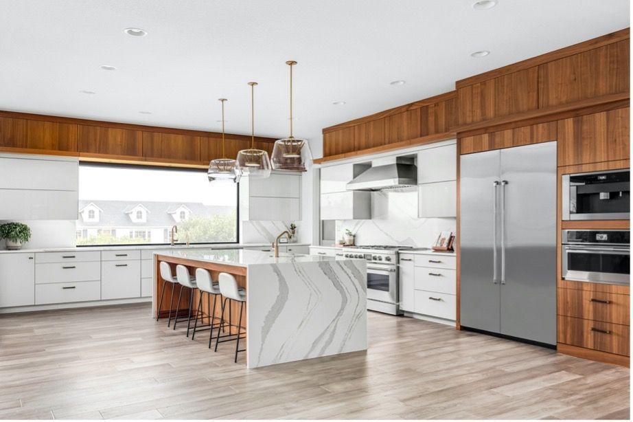 A kitchen with white cabinets , stainless steel appliances , a large island and a large window.