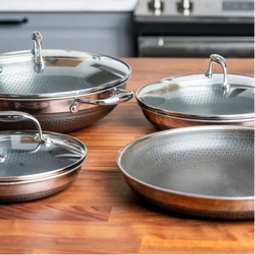 Four stainless steel pans with glass lids on a wooden table