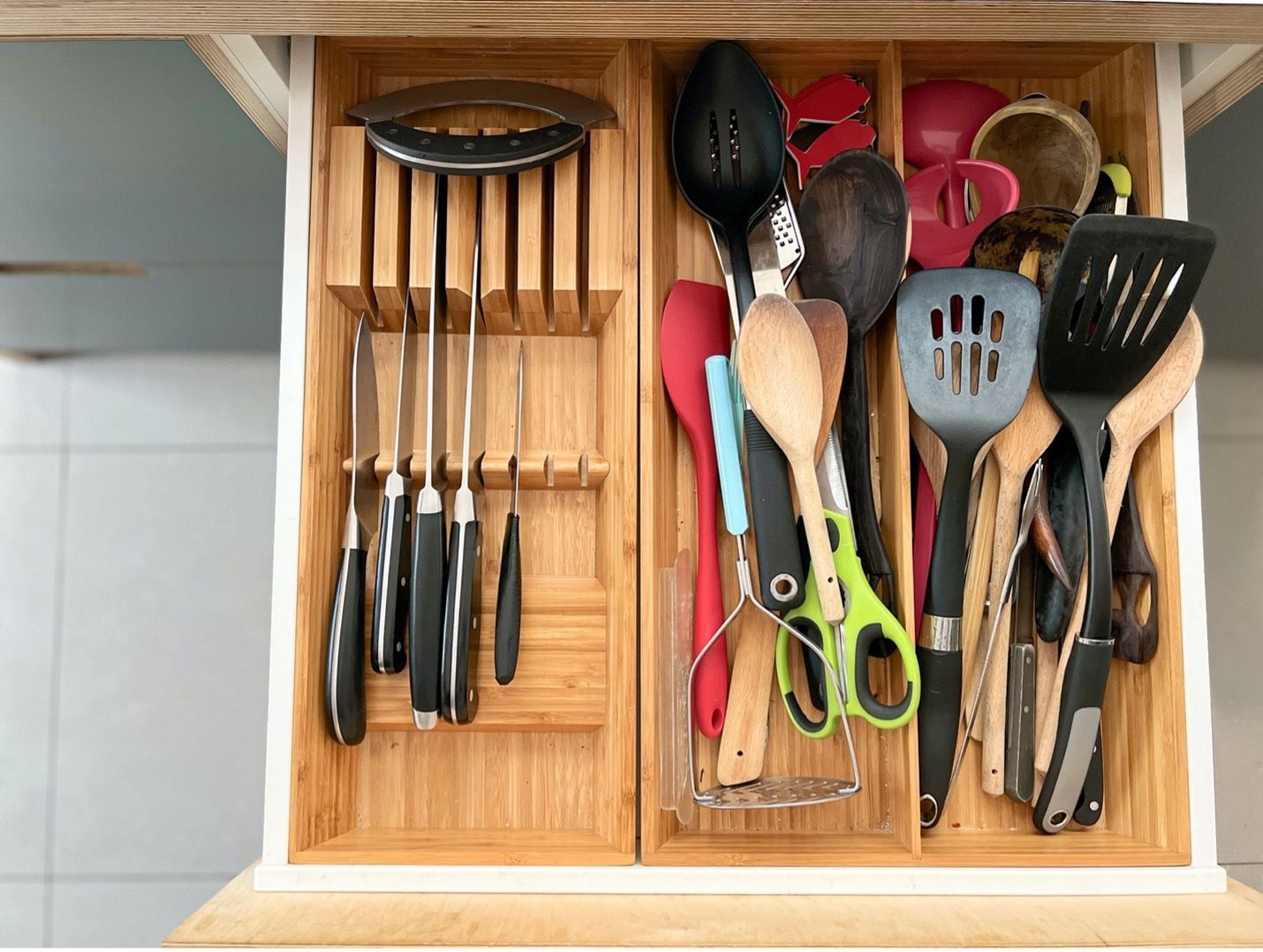 A wooden drawer filled with utensils and knives.
