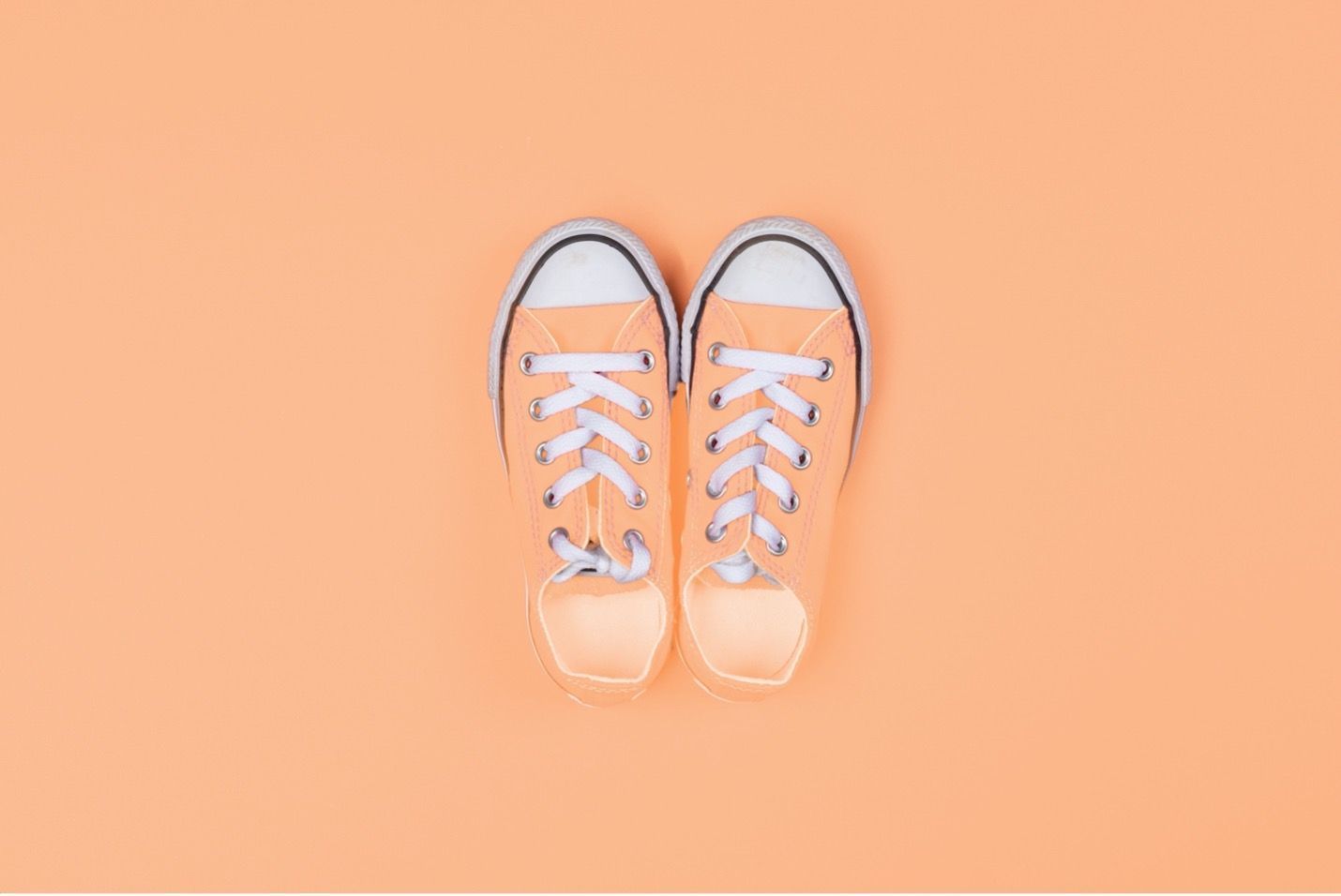 A pair of orange sneakers on an orange background.