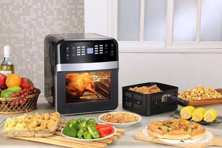 An air fryer is sitting on a counter next to plates of food.