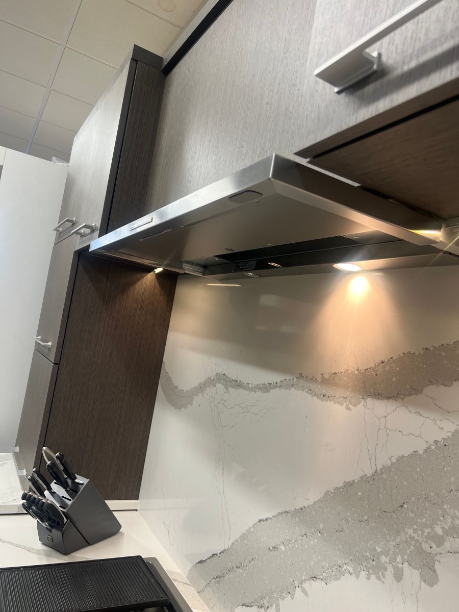 Kitchen range hood over countertop with under-cabinet lighting and a textured backsplash in Cincinnati, OH
