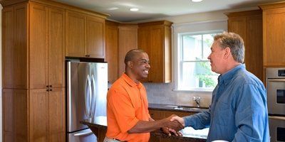 Two men are shaking hands in a kitchen.