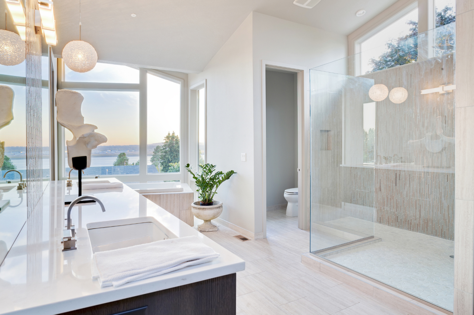 A bathroom with a walk in shower , sink , toilet and large windows.