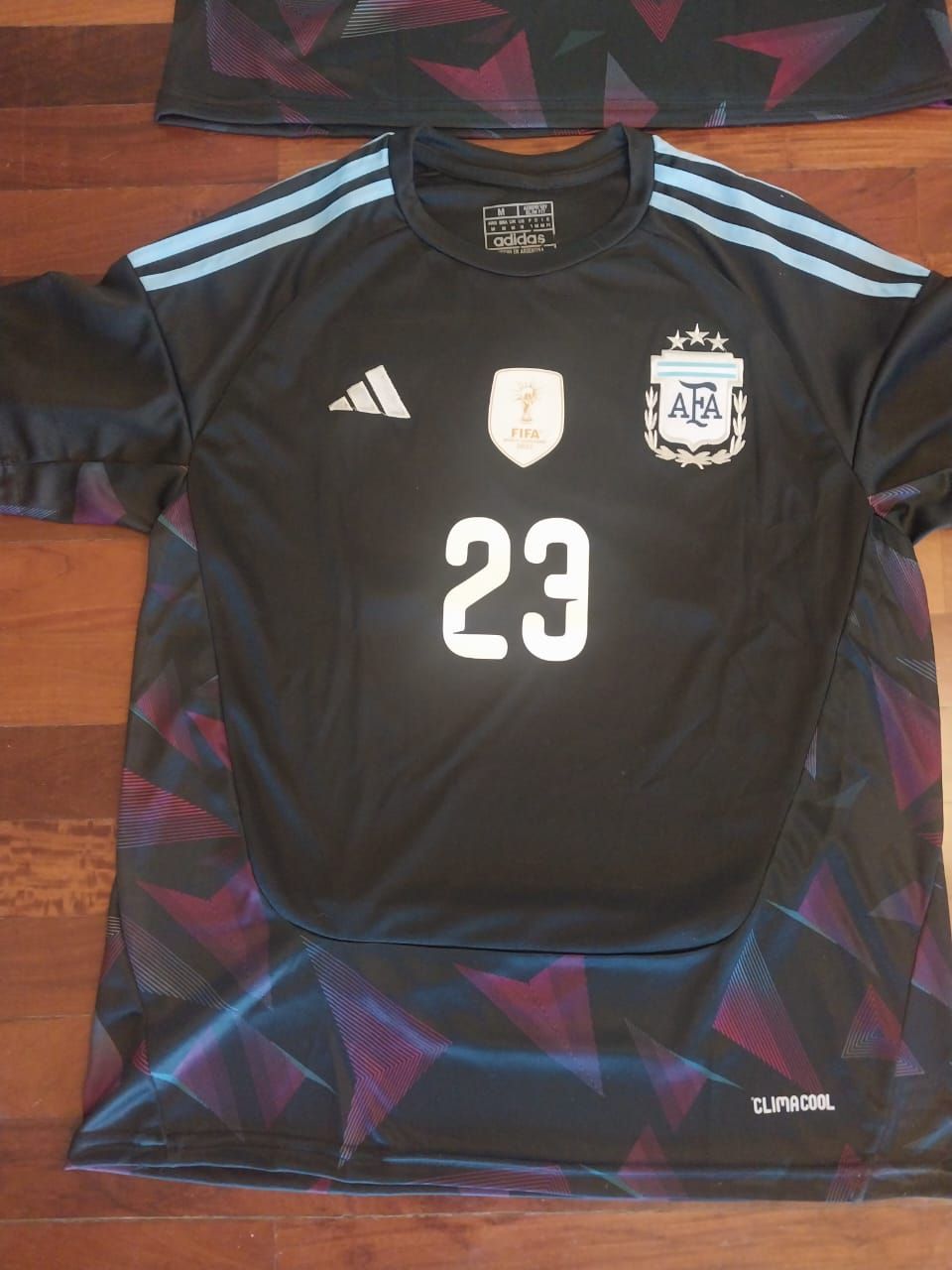 Dos camisetas negras de portero argentino de E. Martínez expuestas sobre un suelo de madera, vistas frontal y trasera.